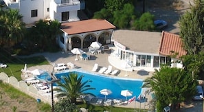 An aerial view of a resort with a swimming pool, lounge chairs, and umbrellas.