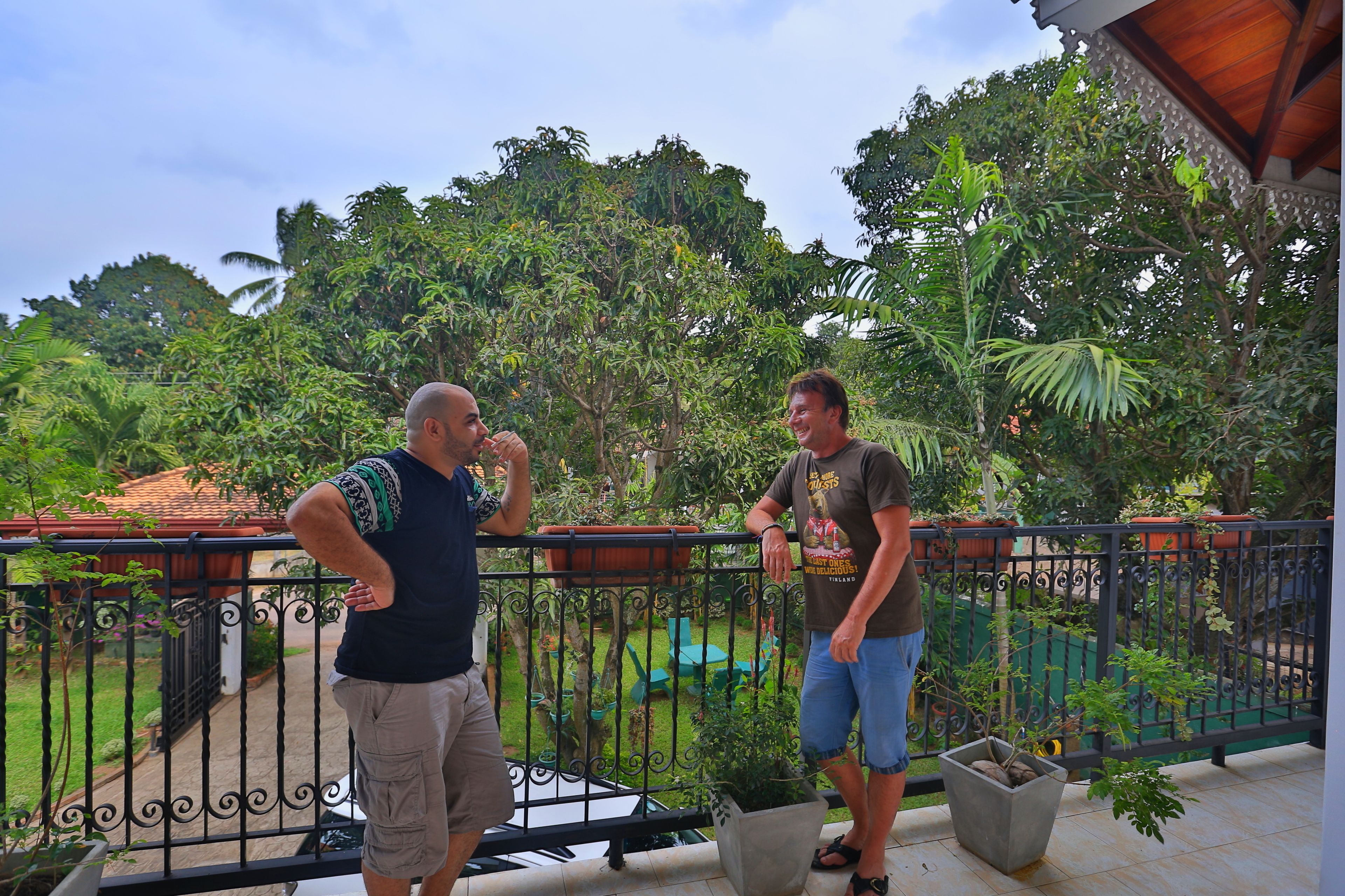 A balcony with a wrought iron railing, potted plants, and a view of a lush garden.