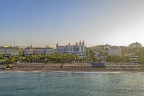 A coastal hotel with multiple buildings, a beach with rows of sun loungers, and palm trees. - Leodikya Kirman Premium - Ultra All Inclusive (Alanya)