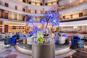 En hotellobby i flera nivåer med ett stort, runt bord i mitten, sittgrupper och en bar.