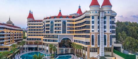 Un hotel con una piscina amplia, varios balcones y torres con techos rojos.