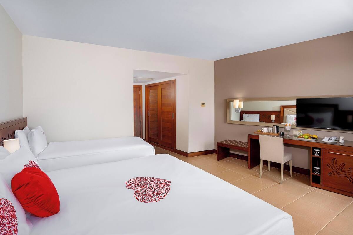 A hotel room with two beds, a desk, a TV, and a bathroom visible through an open door.