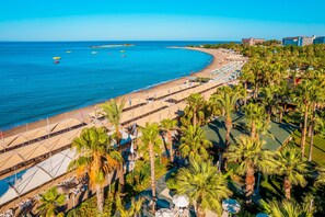 Un complex turístic a la platja amb piscina, palmeres i vista a l'oceà.