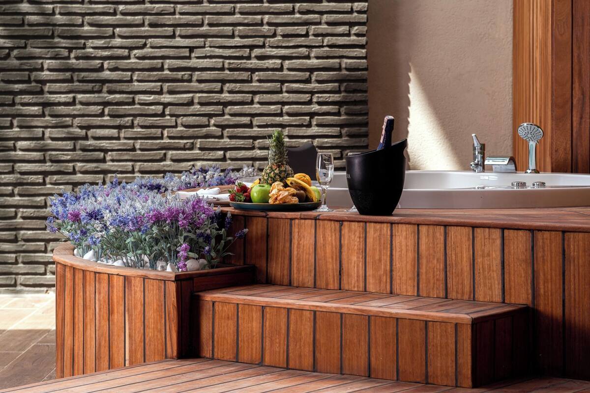 A wooden bench with a planter of flowers and fruits, a black bucket, and a bathtub with a showerhead.