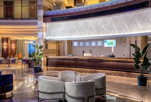 Un hall d’hôtel comprenant un comptoir d’accueil, un espace salon et des panneaux muraux décoratifs.