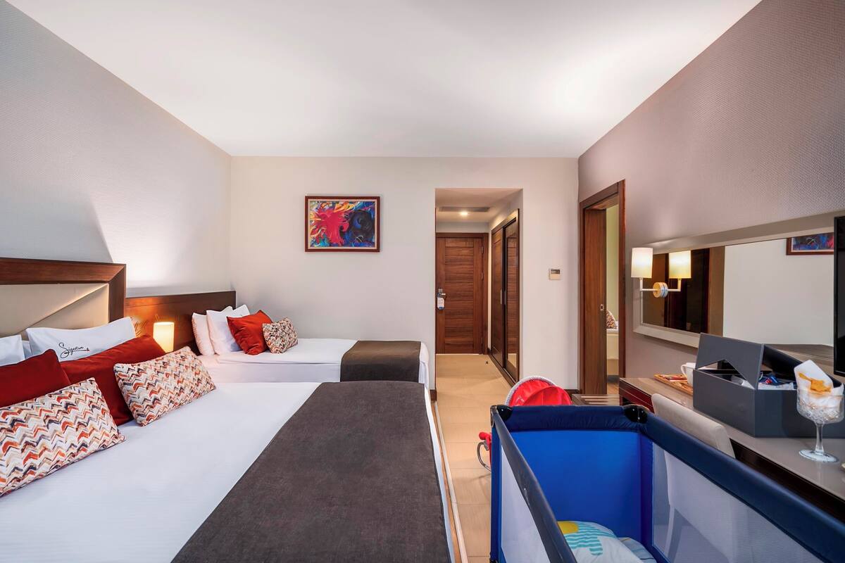 A hotel room with two beds, a desk, a mirror, and a door leading to another room.