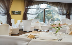 A dining area with white tables and chairs, a vase with flowers, and a painting on the wall.