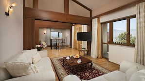 Una sala de estar amplia con un televisor de pantalla plana grande, una zona de comedor con mesa y sillas, y vistas al exterior a través de grandes ventanales.