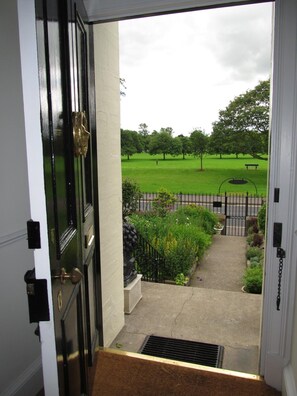 A view from a door to a backyard with a lawn, a bench, and a metal fence. - The Townhouse (Perth)