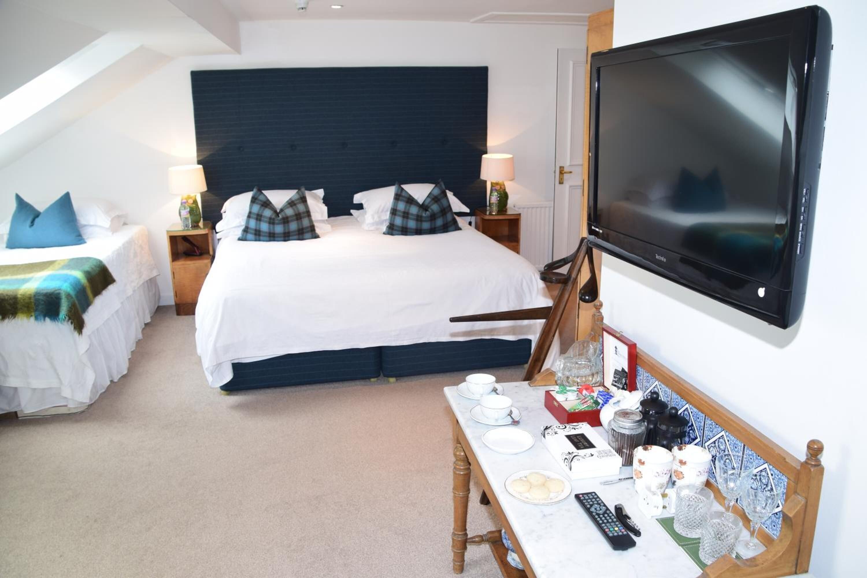 A hotel room with a large bed, a TV, a small table with cups and a remote, and a window with a view of the sky.