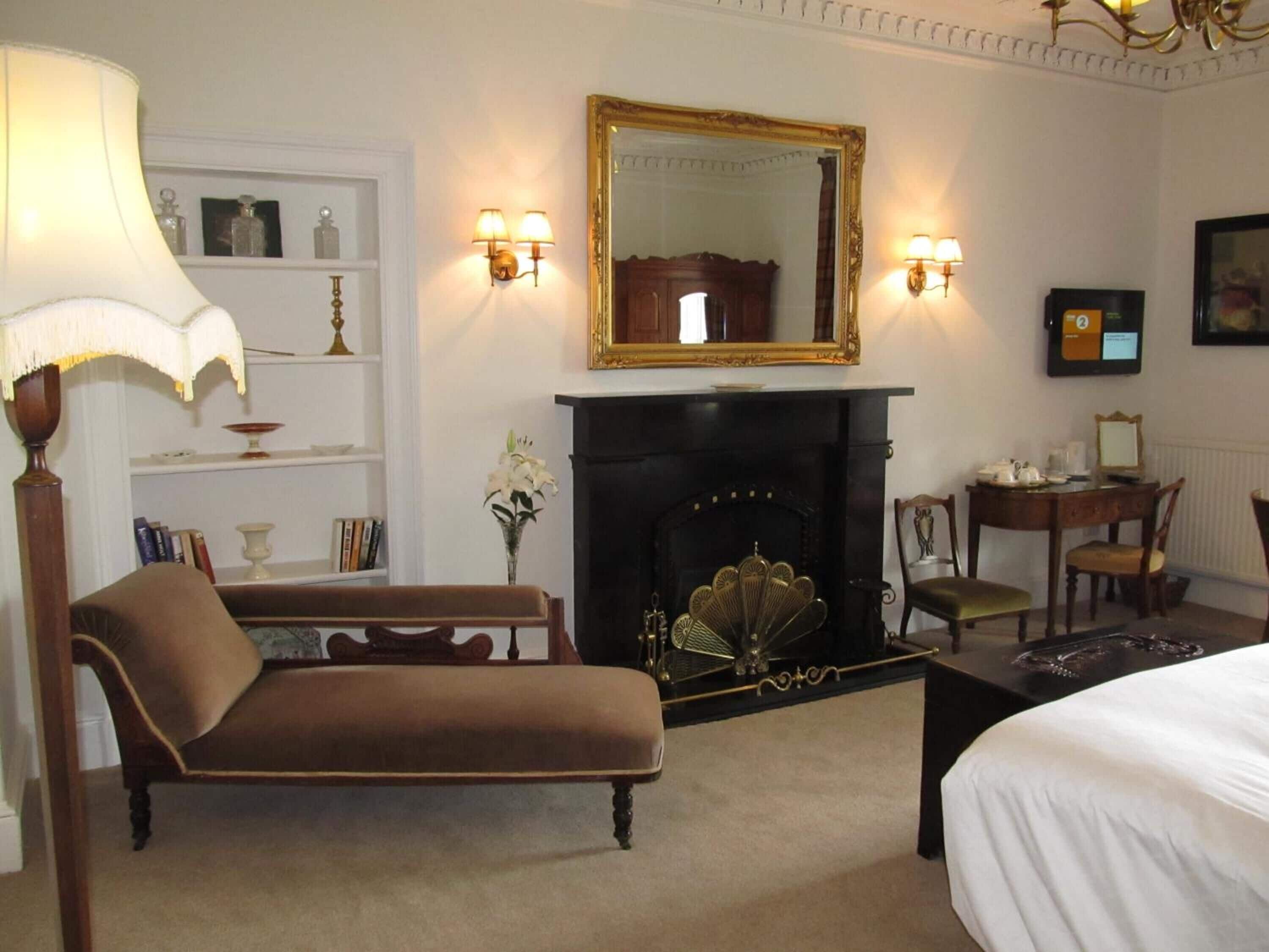 Habitación de hotel con chimenea, sofá, cama, escritorio con silla y televisor.