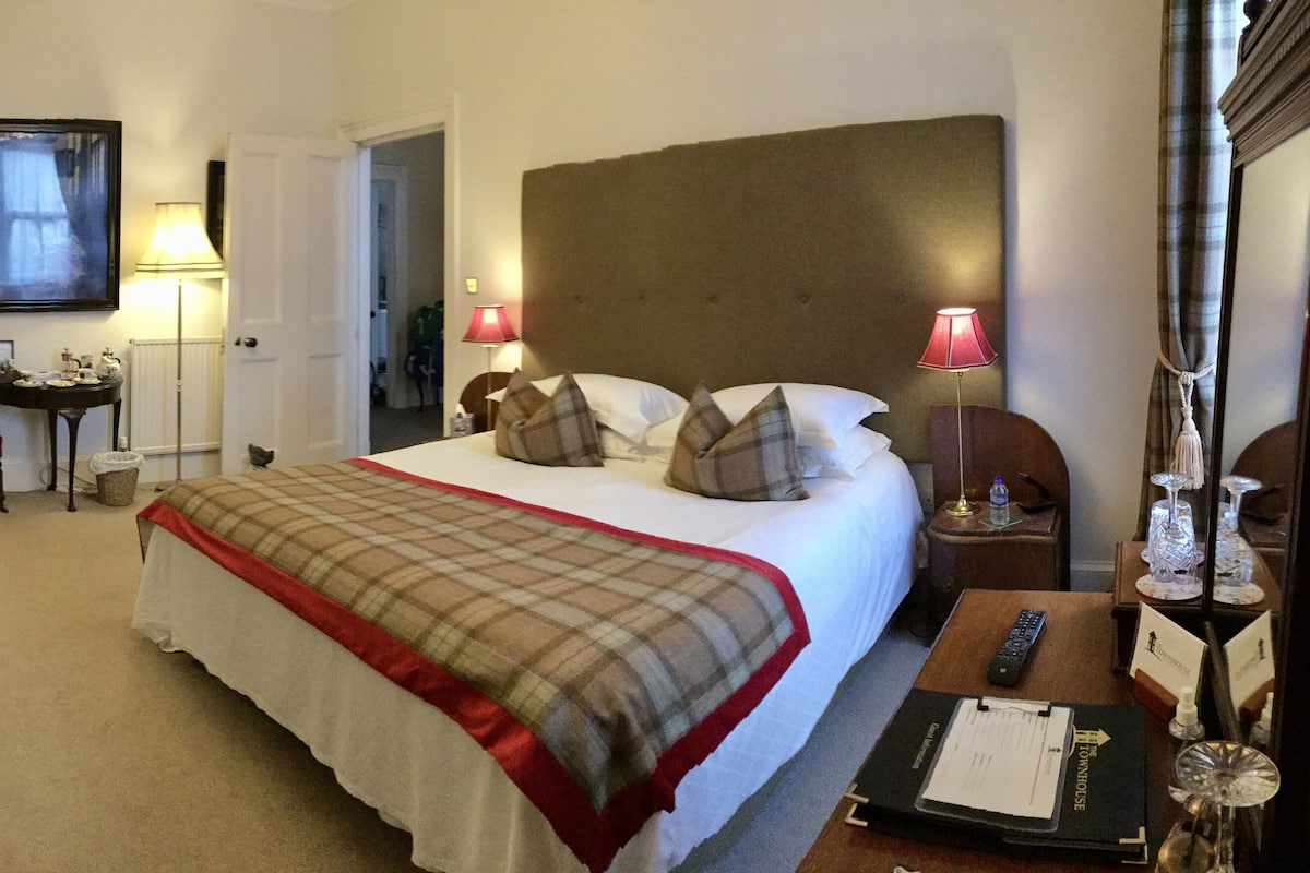 Una habitación de hotel con cama, mesitas de noche, un escritorio, una silla y una lámpara.