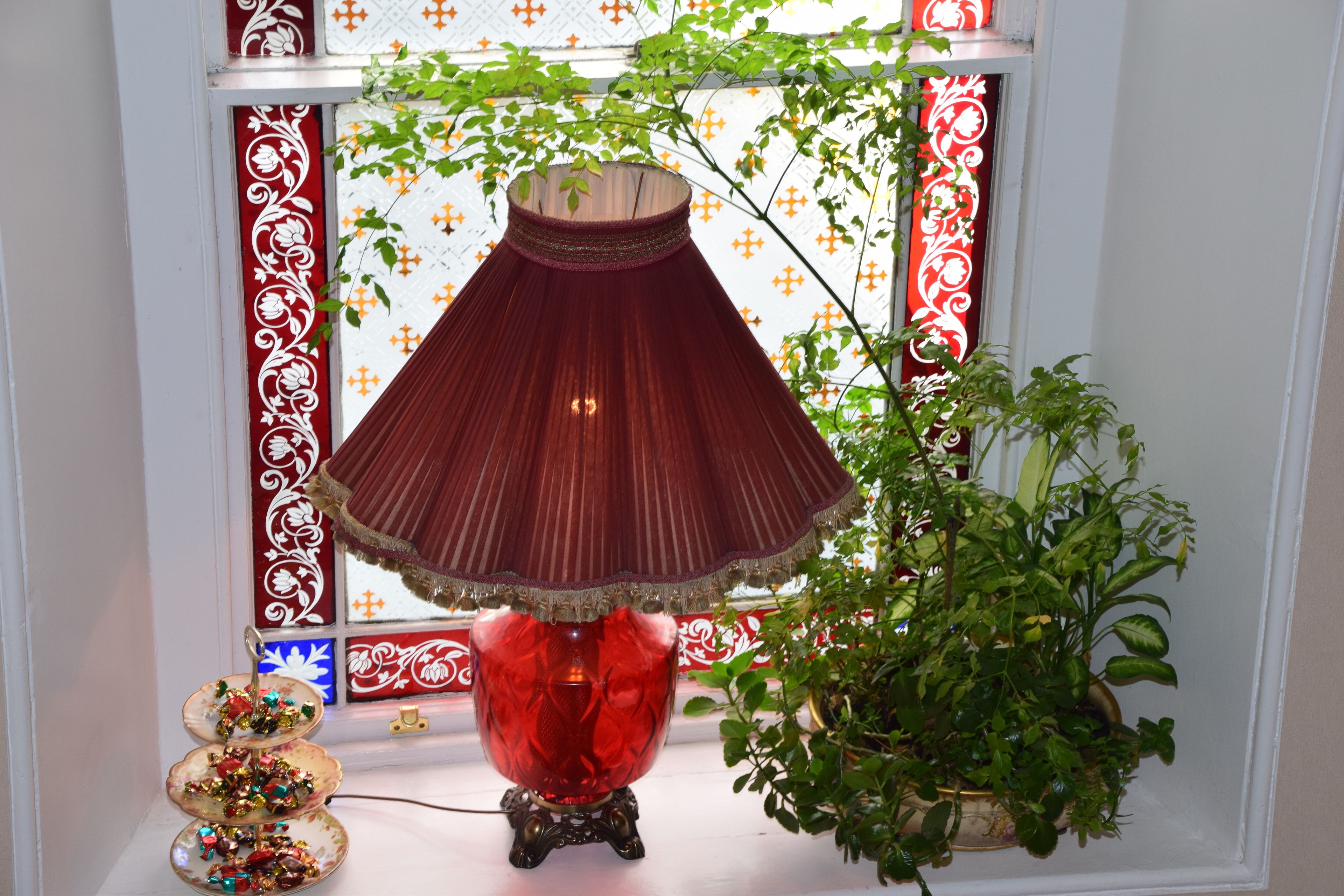 Una lámpara roja sobre un soporte, una planta en maceta y un adorno en el alféizar de una ventana.