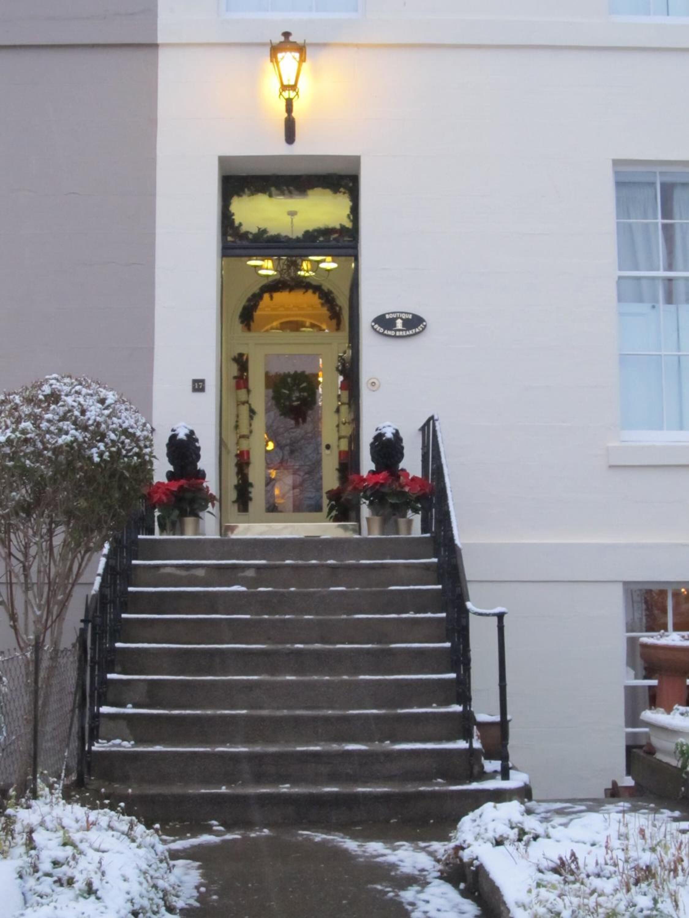 A building entrance with a staircase leading to a door decorated with wreaths and red flowers.
