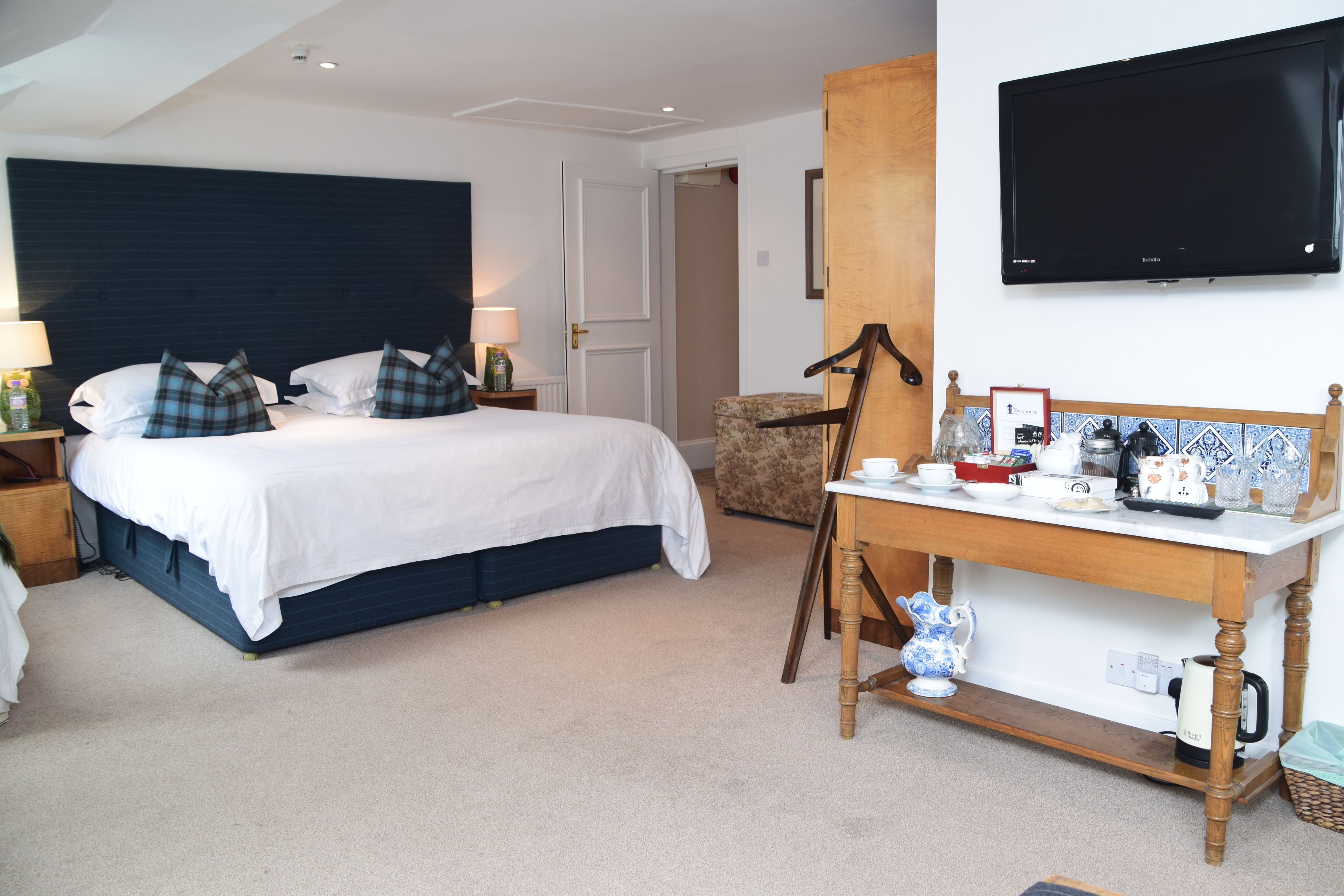 A hotel room with a large bed, a wooden nightstand, a table with tea set, and a television on the wall.