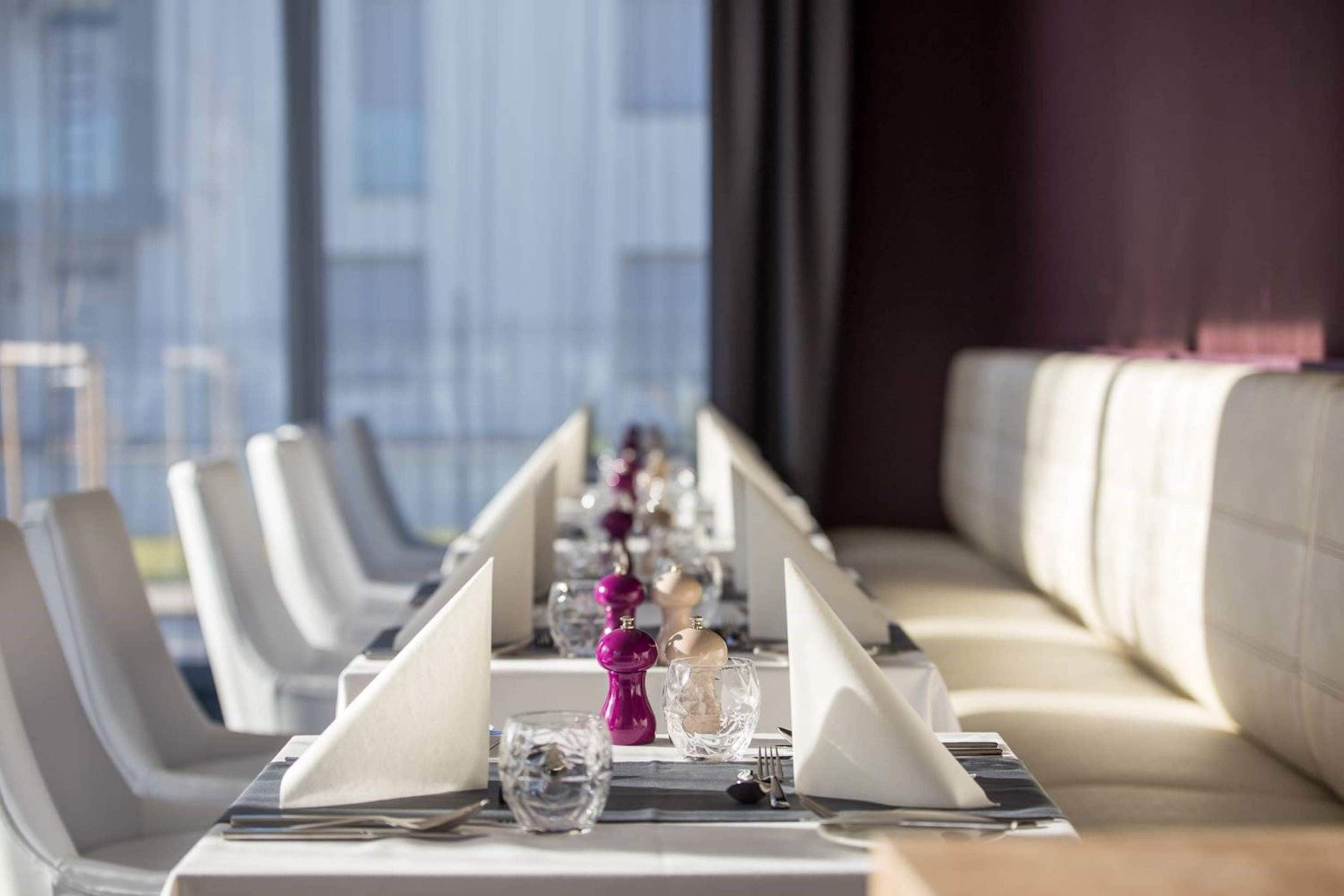 A restaurant setting with a long table, neatly set with plates, glasses, and cutlery.