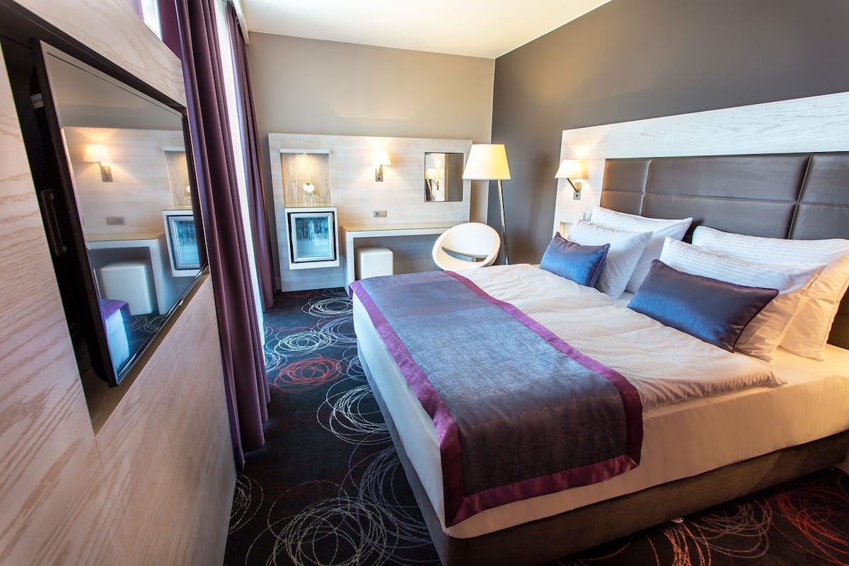 Una habitación de hotel con una cama grande, un escritorio, una silla y un espejo.