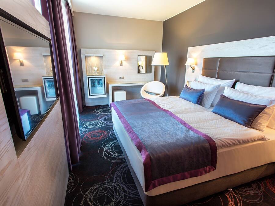 A hotel room with a large bed, a desk, a chair, and a mirror.
