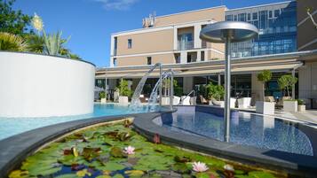 Un hôtel moderne doté d’une piscine, d’un bassin orné de nénuphars et surplombant un ciel d’un bleu limpide.