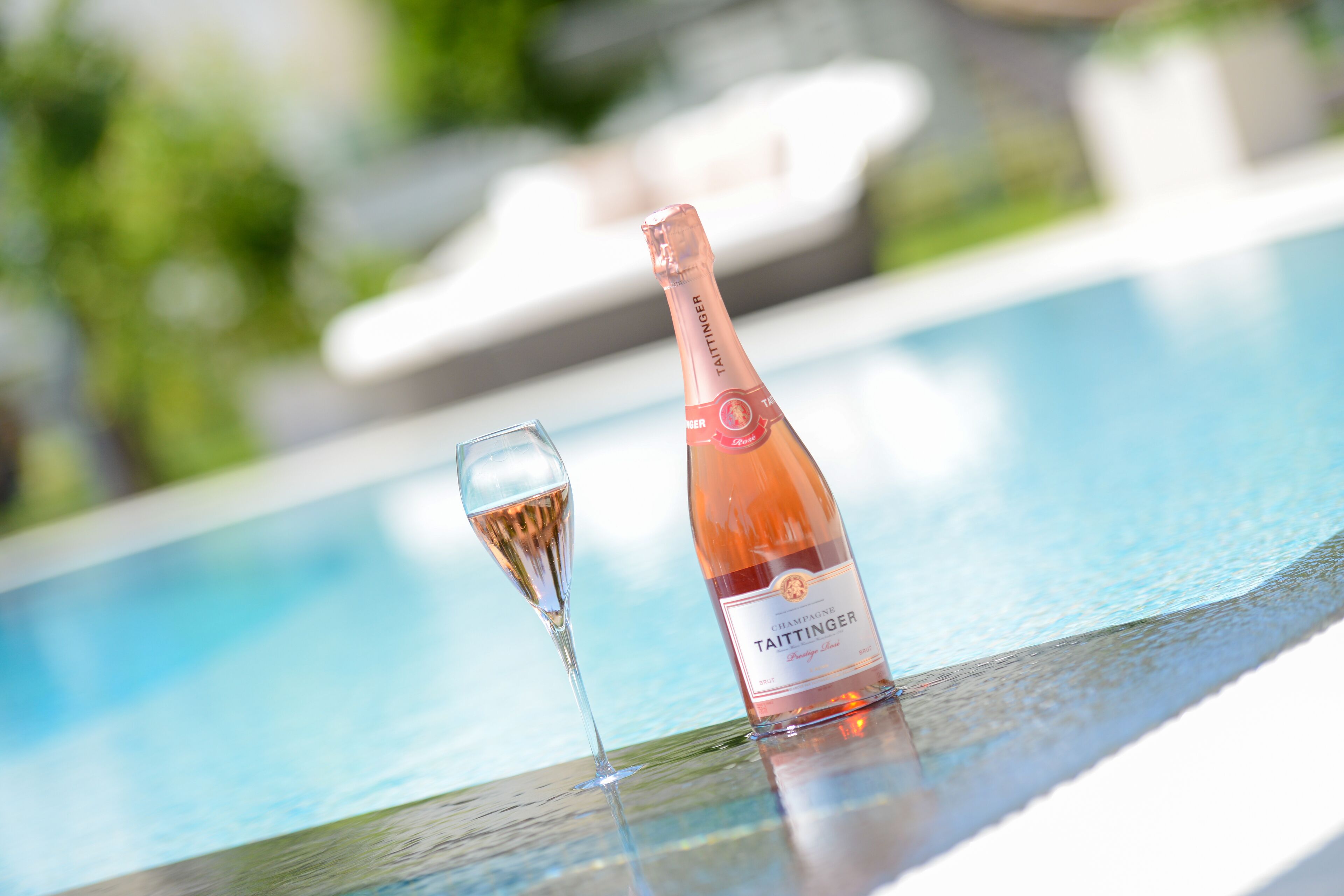 A bottle of Taittinger champagne and a glass on a poolside table.