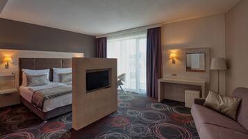 A hotel room with a bed, a desk, a TV, a sofa, and a window with curtains.