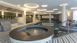 Un área interior de piscina moderna con jacuzzi, sillones de descanso y suelo de baldosas.