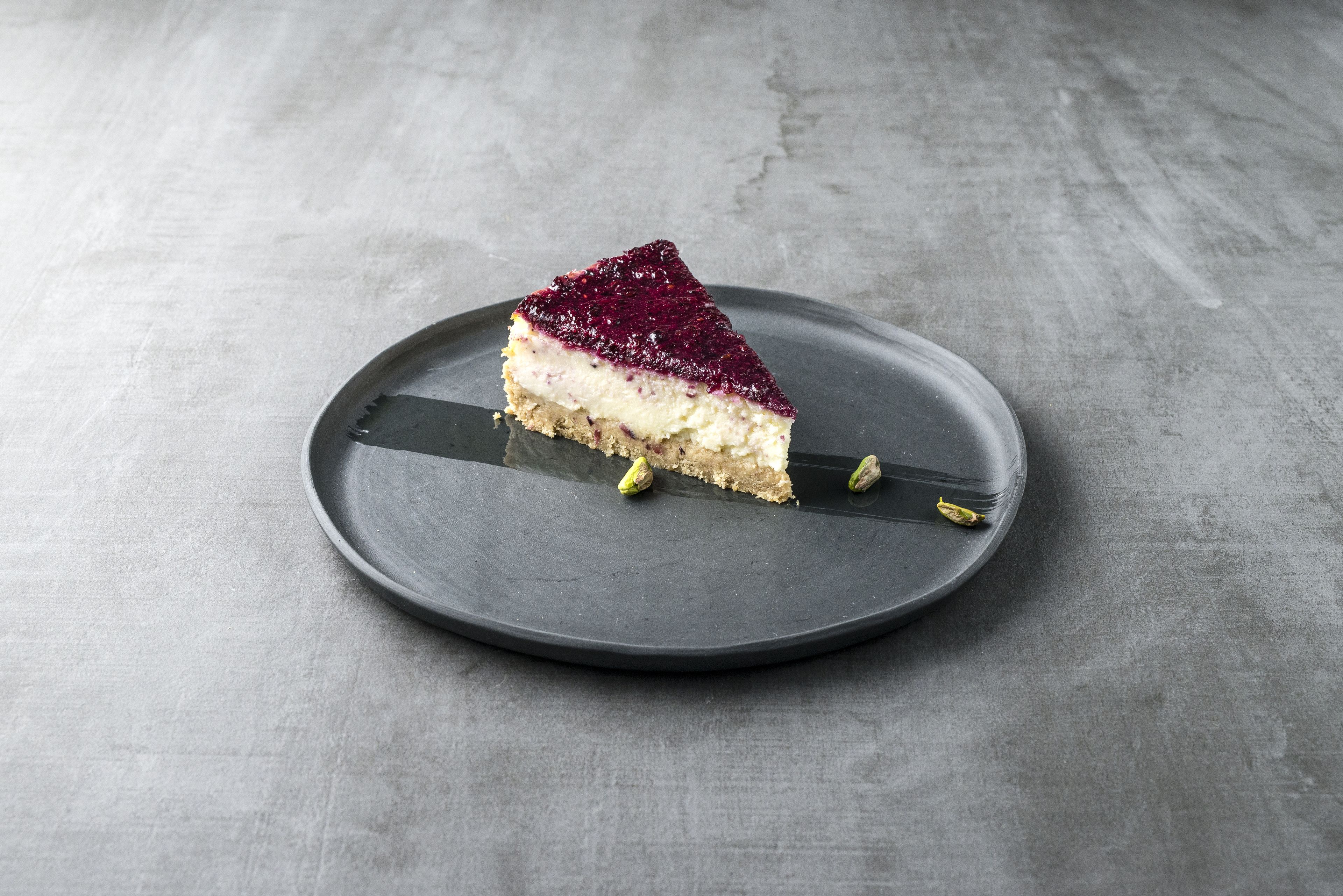Une part de gâteau au fromage sur une assiette sombre, le tout sur un fond texturé.