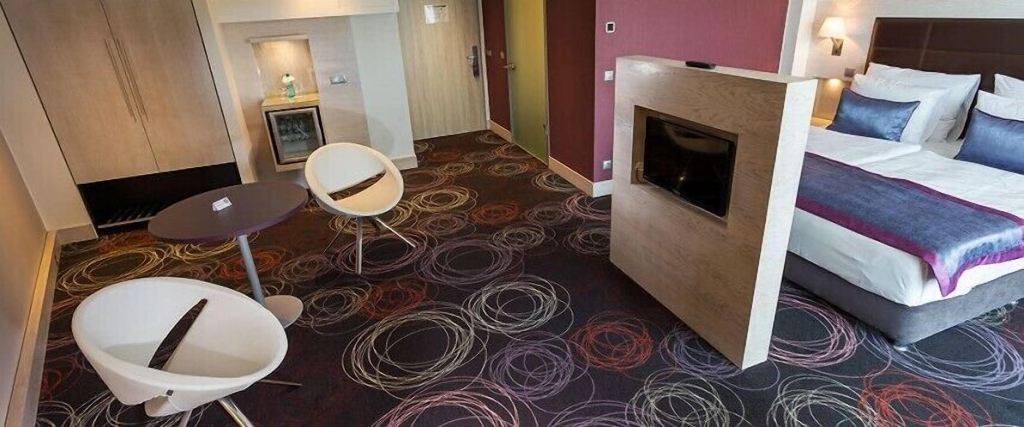 A hotel room with a bed, a small seating area with a table, a fireplace, and a bathroom with a shower.