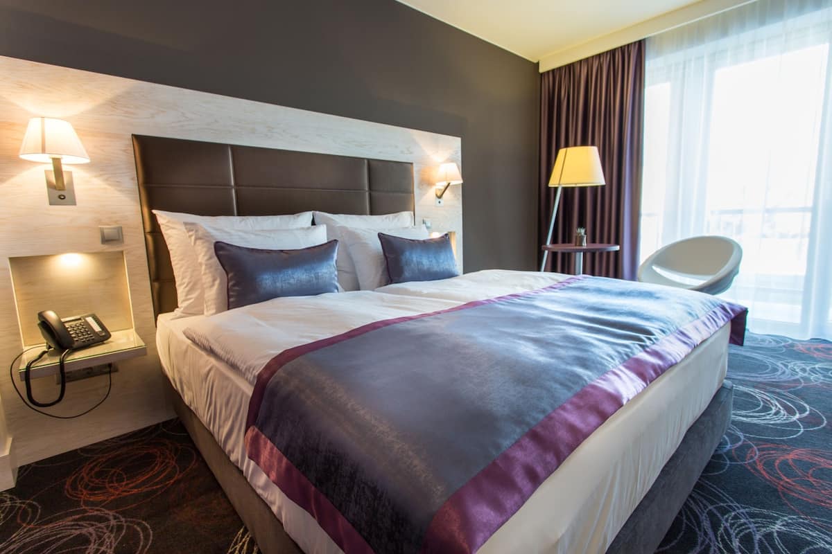 Una habitación de hotel con una cama grande, un teléfono en la mesita de noche, una lámpara y una silla.