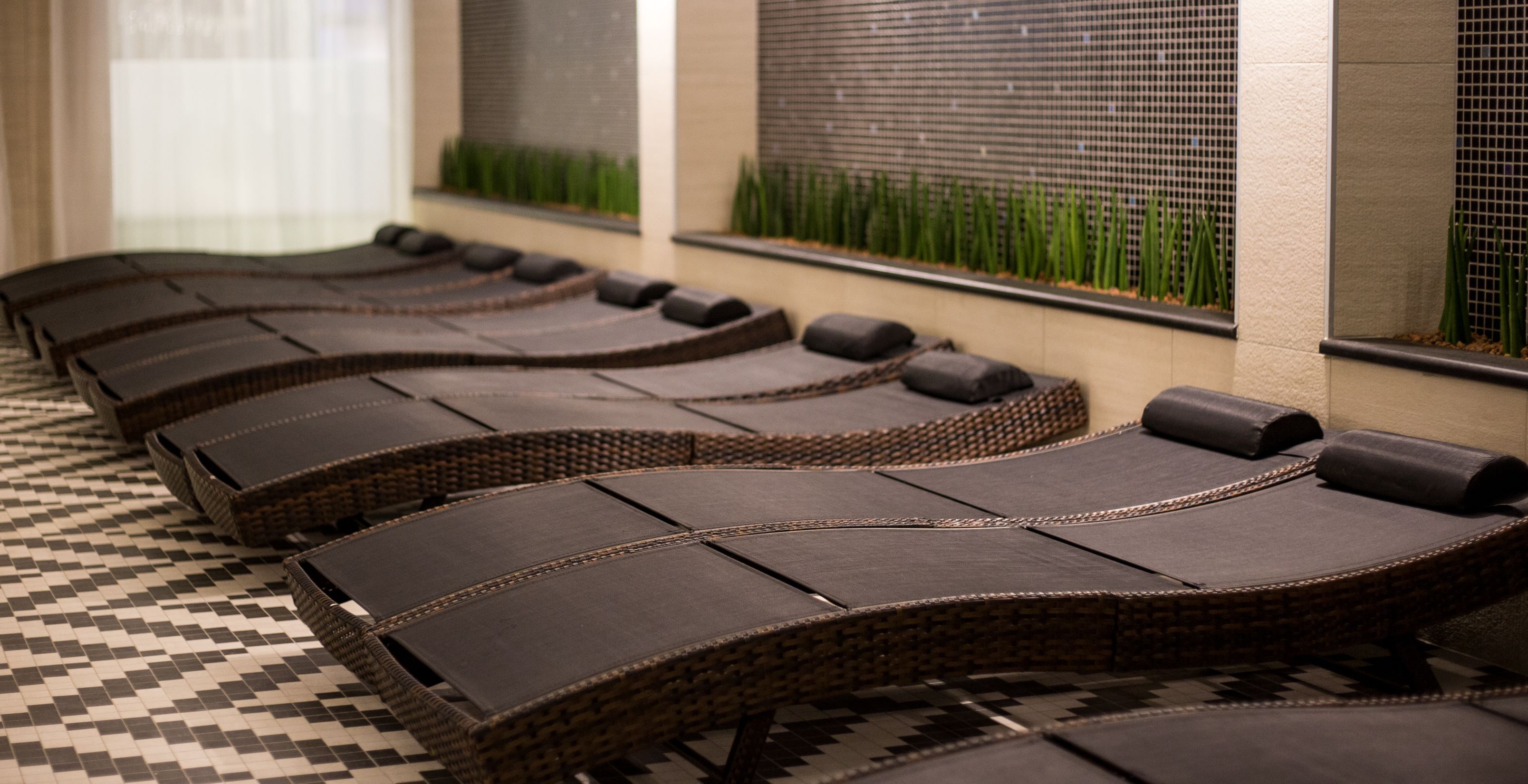 A row of massage chairs with a checkered floor and a wall with a grid pattern and green plants.