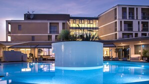 Una piscina con una isla circular, rodeada de sillas de descanso y un edificio con varios balcones al fondo.