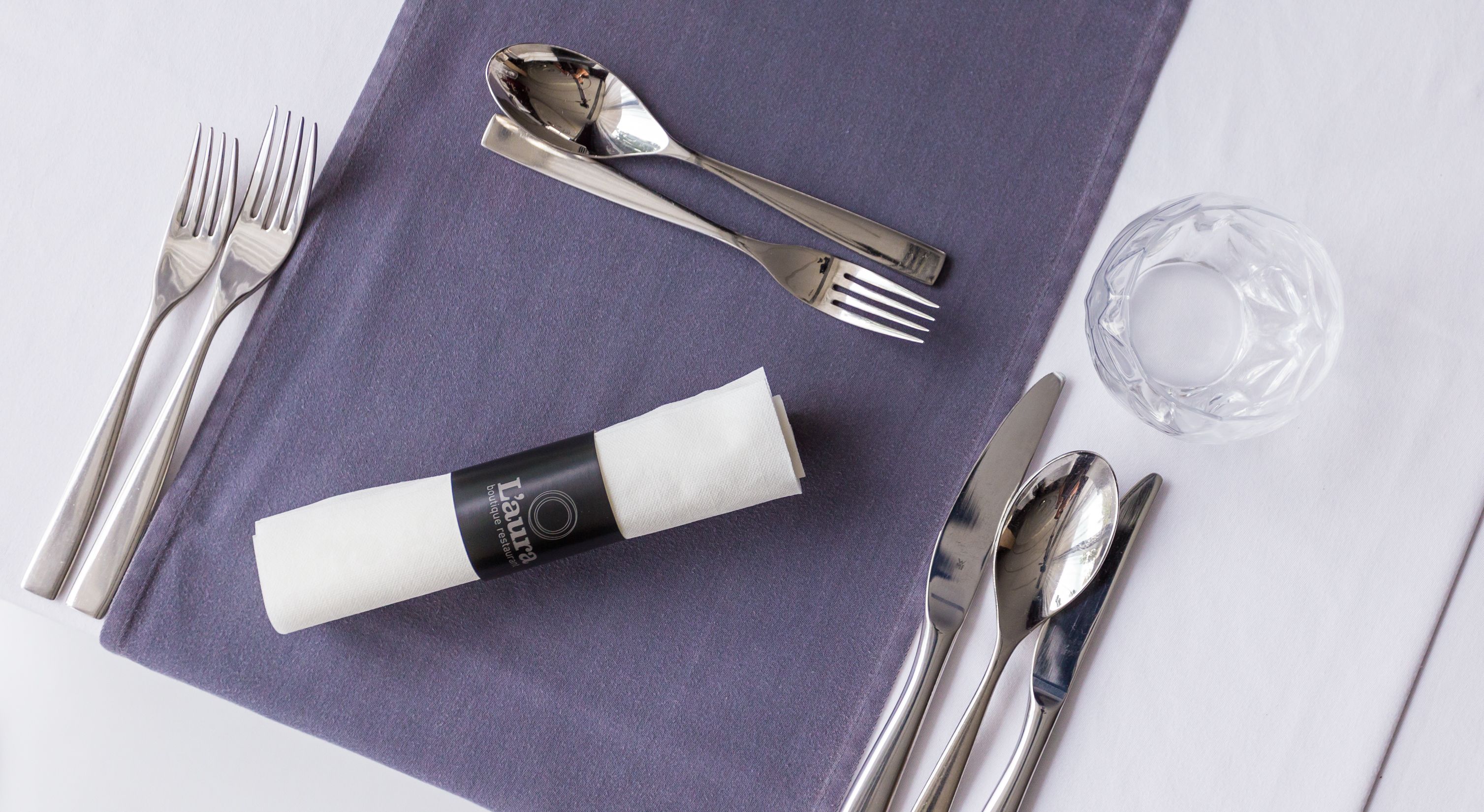 Una mesa bien dispuesta con un mantel individual morado, cubiertos y una copa.