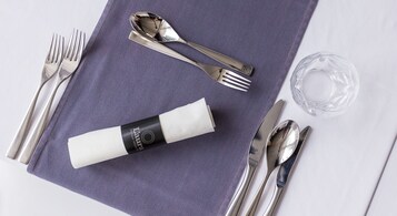 Una mesa bien dispuesta con un mantel individual morado, cubiertos y una copa.