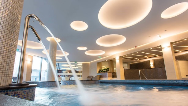 Un área de piscina interior moderna con fuente de agua, iluminación empotrada y pared de azulejos.