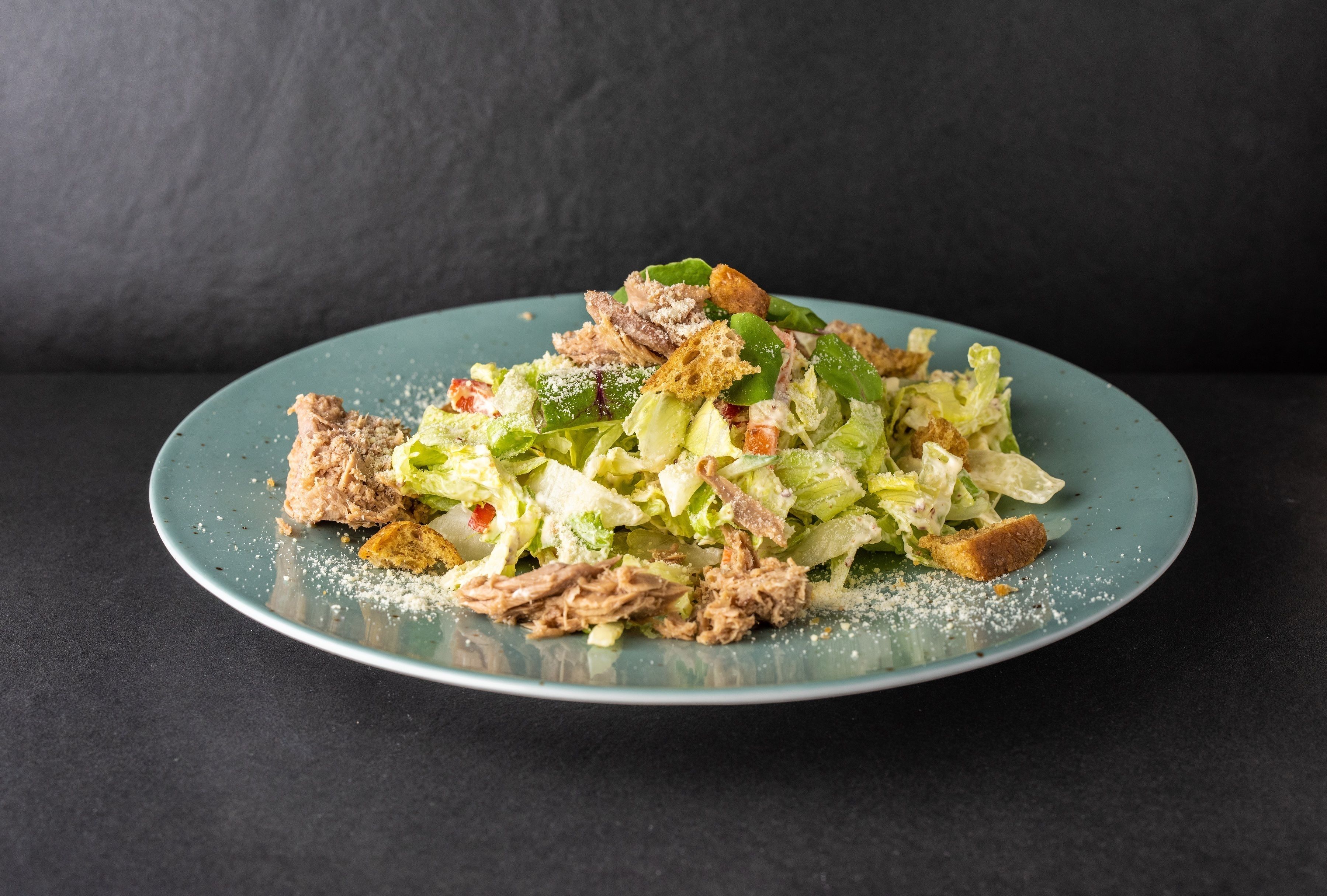 A plate of shredded meat and lettuce salad with croutons on a teal plate.