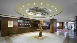 A hotel lobby with a reception desk, a large stained glass ceiling, a wooden sculpture, and a clock. - St. Spas Hotel & Balneo Complex (Velingrad)