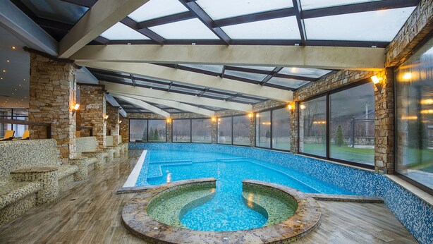 An indoor swimming pool with a glass ceiling, stone walls, and seating areas. - St. Spas Hotel & Balneo Complex (Velingrad)