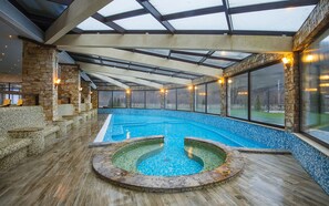 Una piscina interior con techo de cristal, paredes de piedra y zonas de estar.