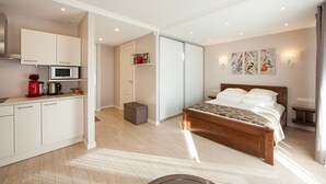 Une chambre d’hôtel moderne avec un lit en bois, une kitchenette, un placard à portes coulissantes et des œuvres d’art accrochées aux murs.