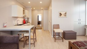 Un espace de vie compact comprenant un coin cuisine, un coin repas et un coin salon avec un canapé et un pouf.