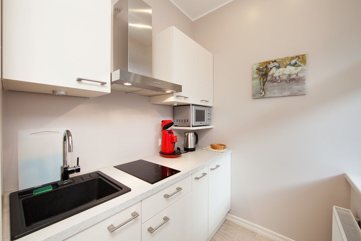 Une cuisine moderne avec des meubles blancs, une hotte de cuisinière en acier inoxydable, un four à micro-ondes et une machine à café rouge.