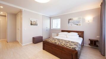 A bedroom with a wooden bed, a small bedside table, a nightstand, a window, and a door leading to another room.