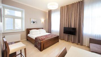 Habitación de hotel con cama, televisión, escritorio y ventana con persianas.