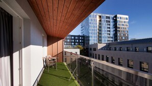 Un balcon avec un revêtement de sol en gazon synthétique, un plafond en bois et une vue sur des immeubles modernes.