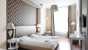 Habitación de hotel con dos camas, un escritorio, un televisor y un papel tapiz estampado.