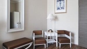 Una habitación pequeña con un banco, dos sillas, una mesa, una lámpara y un cuadro en la pared.