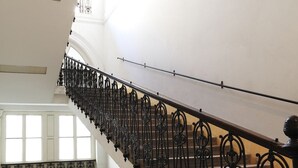 Una imponente escalera con barandales de metal negro ornamentado, que conduce a un piso superior con amplias ventanas.