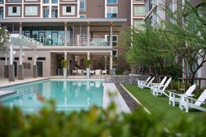 A hotel with a swimming pool, outdoor seating, and a covered area with tables and chairs.