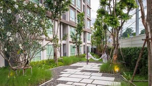 A pathway leading to a building with multiple floors, surrounded by greenery and trees. - Baan Peang Ploen by Montri (Hua Hin)