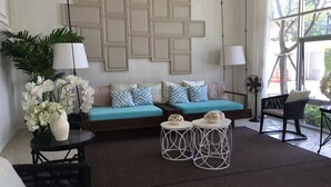 A modern living room with a teal sofa, patterned cushions, a white vase with flowers, and a geometric wall design. - Baan Peang Ploen by Montri (Hua Hin)